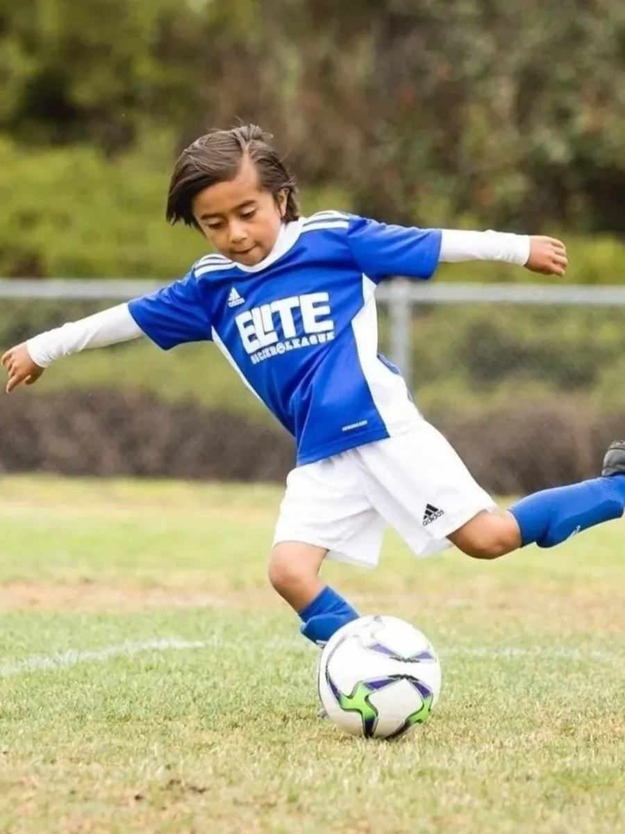 Young Elite Soccer League player in a blue ESL kit striking the ball during a game